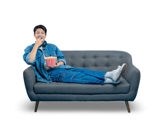PNG,An amused young man laughs and eats popcorn while lounging on a sofa, enjoying a comedy movie at home.
