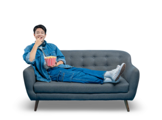 PNG,An amused young man laughs and eats popcorn while lounging on a sofa, enjoying a comedy movie at home.
