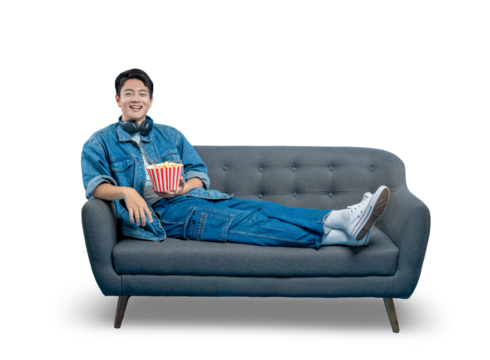 PNG,A relaxed young man lounging on a sofa reaches for popcorn while watching a movie or TV show.
