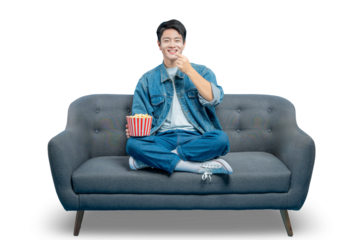 PNG,An amused young man smiles as he eats popcorn from a striped bucket while enjoying a show on his couch.
