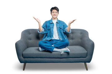 A friendly young man sits on a sofa with his arms open wide in a welcoming or presenting gesture. Isolated on a PNG background.
