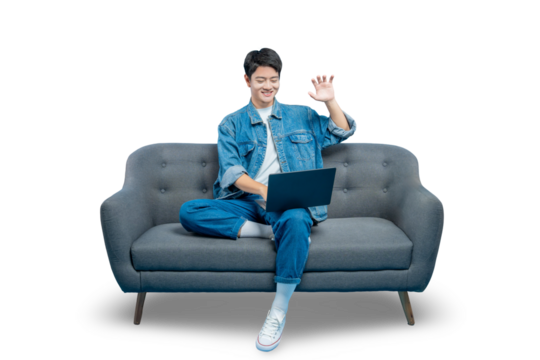 A happy young man makes a peace sign while using his laptop on a sofa, possibly during a video call or a study break.PNG