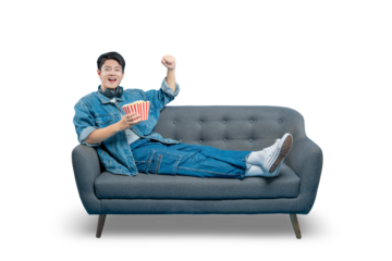 A smiling young man in a denim jacket relaxes on a sofa with a bucket of popcorn, enjoying a day of leisure at home.
PNG