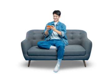 A happy young man in a denim jacket plays a game on his smartphone while relaxing on a sofa.PNG