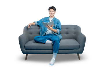 A young man sits comfortably on a sofa, smiling as he reads a book, representing leisure, study, and learning.PNG