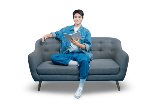 A young man sits comfortably on a sofa, smiling as he reads a book, representing leisure, study, and learning.PNG