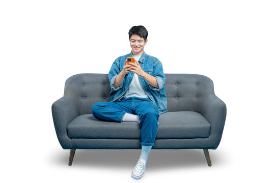 A smiling young man uses his smartphone for texting or social media while relaxing at home on the sofa.PNG
