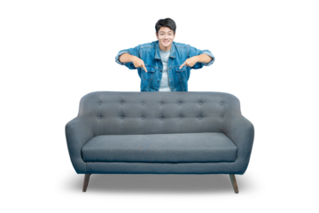 A smiling young man peeks over a sofa and points down at it, as if recommending the furniture or inviting someone to sit.PNG
