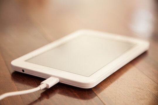 White tablet on wood plugged into the charger