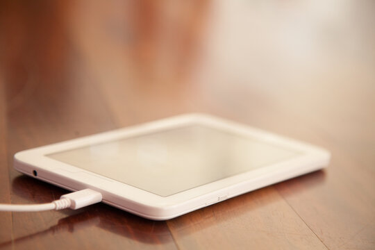 White tablet on wood plugged into the charger
