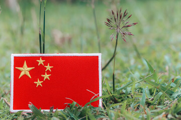 Eco friendly embroidered Chinese flag on fresh grass with small flowers. Horizontal photo with copy...