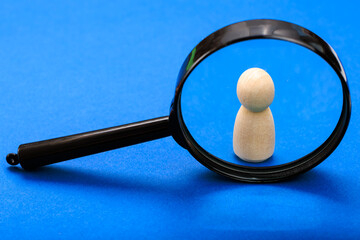 Wooden figure under magnifying glass on blue background