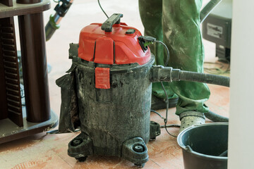 Dusty Red Shop Vac on Concrete Floor During Construction, Renovation, Home Improvement with Worker...
