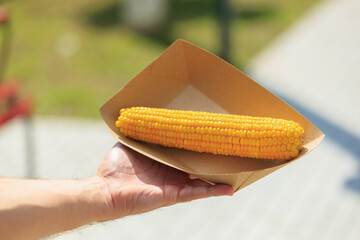 Hand holding grilled corn in cardboard tray outdoors