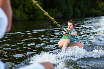 Young beautiful sporty girl in a green life jacket rides a wakeboard on a river or lake near city....
