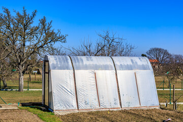 Rural greenhouse in early spring garden setting with clear blue sky