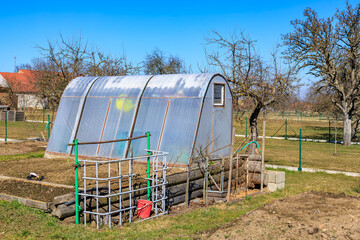 Sunny greenhouse in rural garden setting with bare trees and blue sky