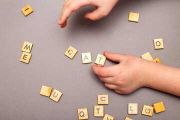 child hand hands collecting word cat from wooden cubes on gray background.