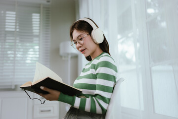 A young woman in a striped shirt and glasses relaxes indoors, enjoying music or a podcast through...