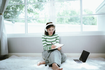 A young woman in a striped shirt and glasses relaxes indoors, enjoying music or a podcast through...