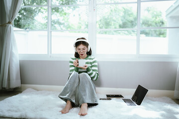 A young woman in a striped shirt and glasses relaxes indoors, enjoying music or a podcast through...