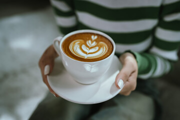 A woman enjoys a hot cappuccino, holding the coffee cup gently with both hands, savoring warmth and relaxation during a peaceful morning coffee break in a cozy café.