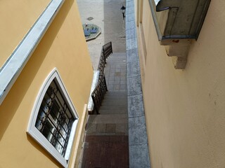 Top view of a narrow alley between yellow buildings with grey tile pavement leading to a staircase...
