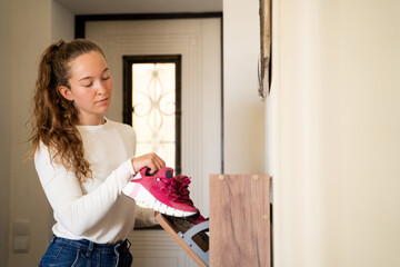 Young woman organizing shoes at home, putting pink sneakers into wooden rack at home, daily routine...