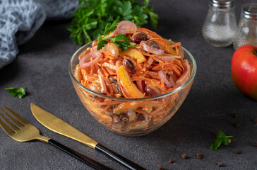 Salad with beans, sausage and carrots in transparent salad bowl on gray table