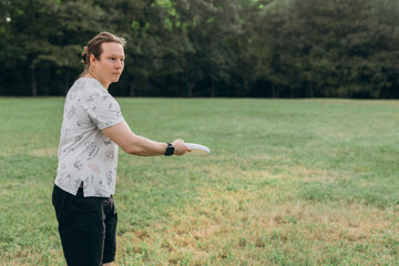 Male athlete with long hair in bun stands sideways holding white frisbee over green grass field...