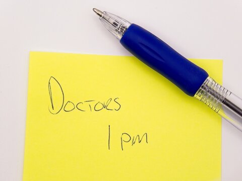 handwritten doctors appointment reminder on yellow sticky note with pen
