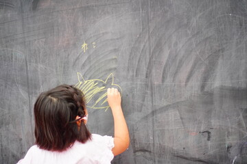 黒板に黄色いチョークで猫の絵を描いている子供の手と創造的な落書き