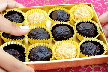 Delightful assortment of handcrafted chocolates with a hand selecting a piece from a wooden box