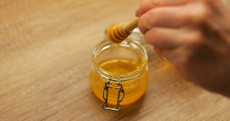 Woman lifts honey dipper from transparent jar to enrich flavor of lemon tea. Soothing drink with...