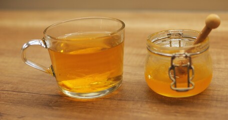 Cut lemon floats in transparent mug of steaming tea infused with honey from jar. Hot drink with natural sweetener helps soothe sore throat during flu