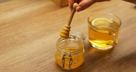 Woman prepares honey dipper removing from jar to complement citrus tea with natural sweetness....