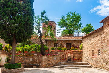 Peaceful monastery courtyard with stone fountain and blooming flowers in Meteora Greece
