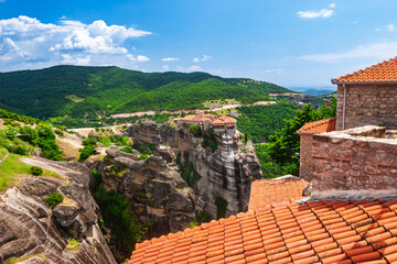 Elevated perspective over orange tiles toward Meteora monasteries on vertical cliffs in Greece