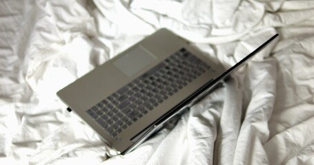Powerful laptop in sleep mode placed on bed with white crumpled blanket in room. Flexible schedule...