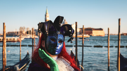 Venice carnival features masked performer by the waterfront during sunset