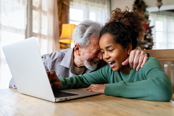 Teenager girl using laptop for education, online gaming, fun, distance learning with grandfather