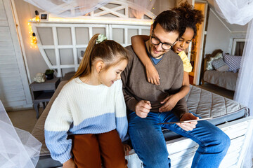 Excited single father plays with diverse, multi-ethnic daughters. Using digital tablet enjoy weekend