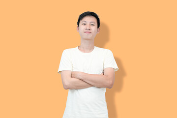 A young Asian man with braces smiles while standing with his arms crossed against a peach background