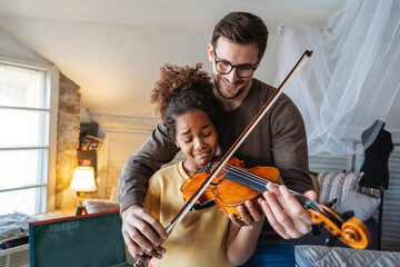 Music is so much fun. Young father teaching his little daughter to play violin and smiling.
