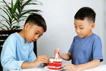 Asian boys sitting at a table eating red velvet cake together. A warm childhood moment perfect for food or family themes.