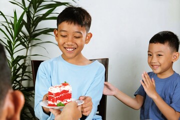 Two cheerful Asian boys enjoying red velvet cake together, sharing laughter and friendship in a...