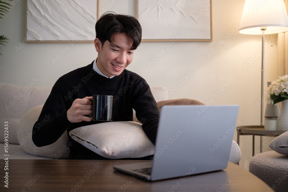 Poster young man drinking coffee while working on a laptop from home. comfortable and cheerful remote worki