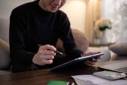 Man working on digital tablet with stylus while reviewing financial documents at home.