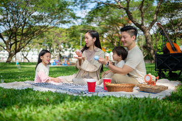 Happy Asian family enjoying a relaxing picnic together in a green park on a sunny day.