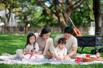 Happy family enjoying a picnic in the park, reading a book and playing with a balloon toy.